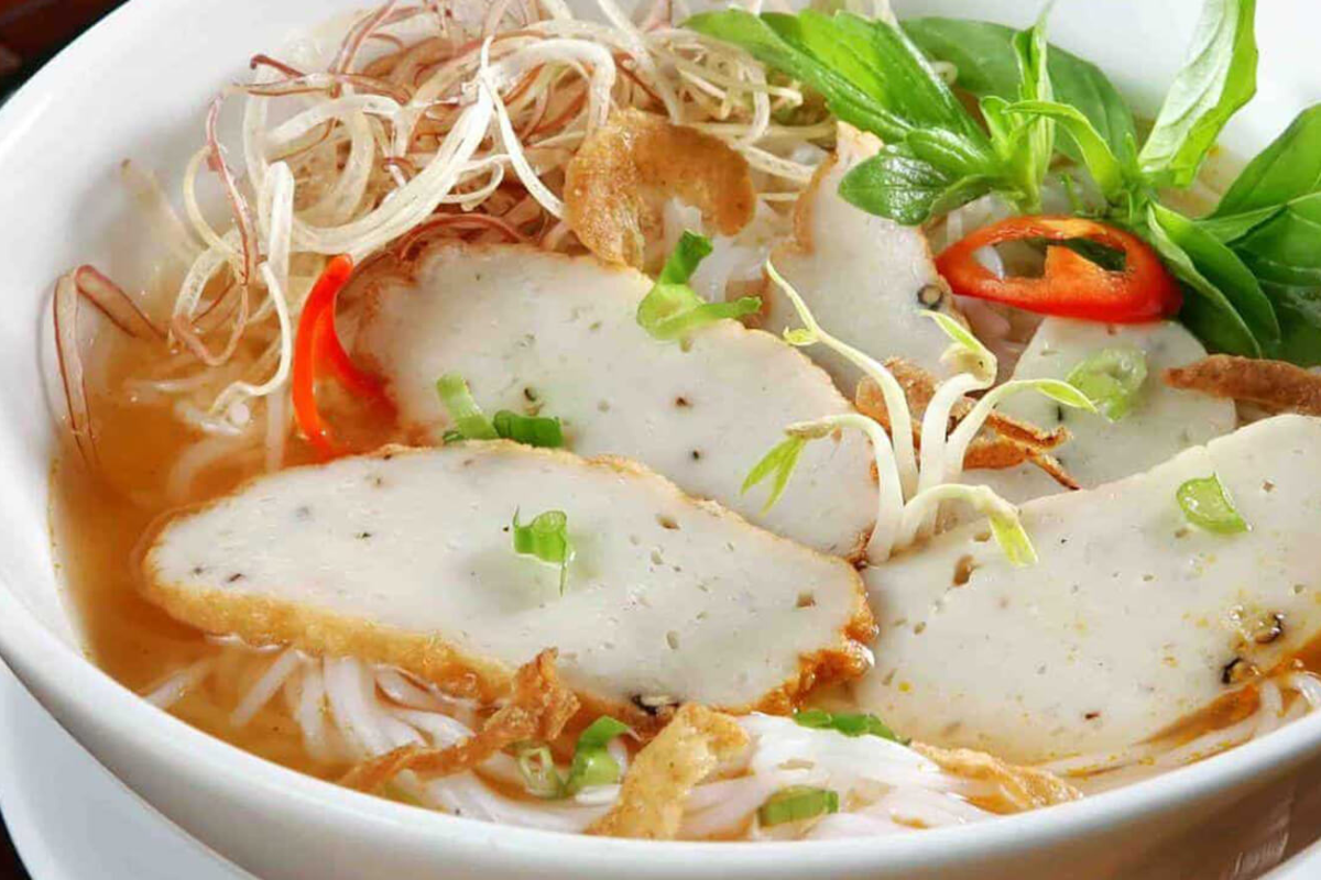 A steaming bowl of fish cake thick noodle soup with herbs