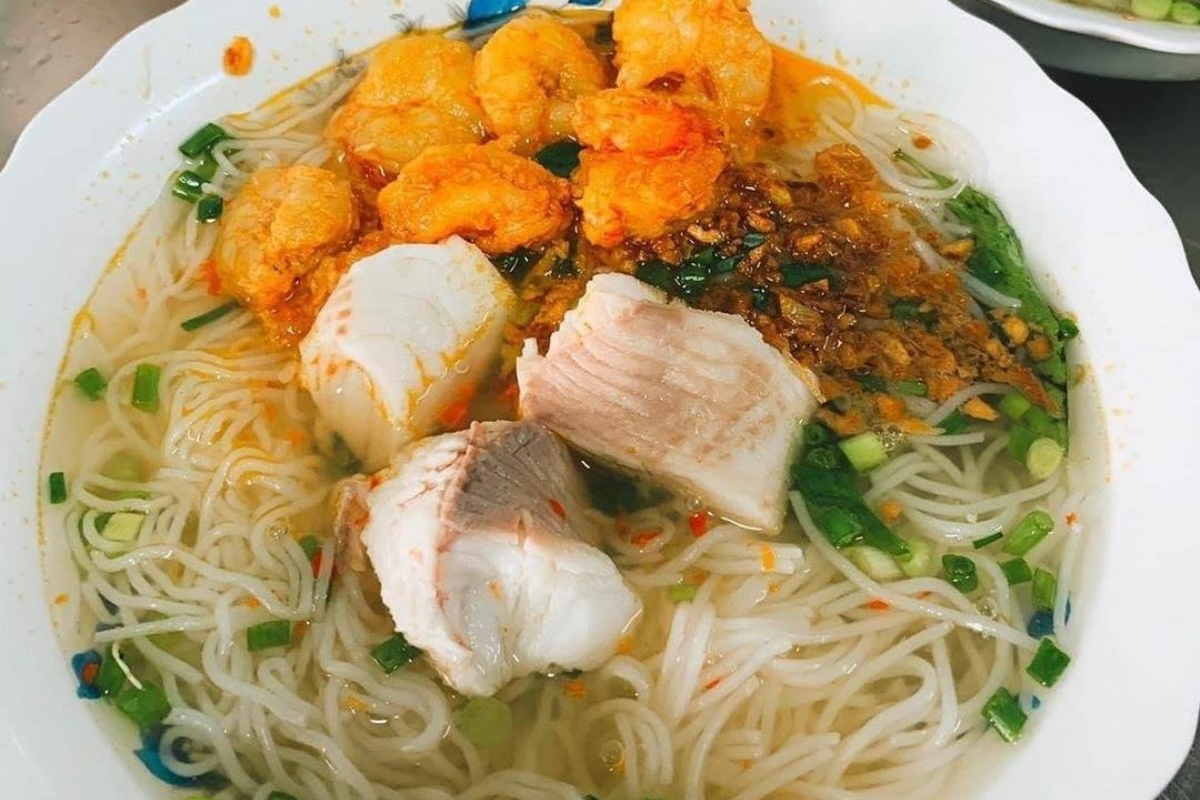 Clear bowl of Bún Cá Kiên Giang garnished with banana blossom and herbs