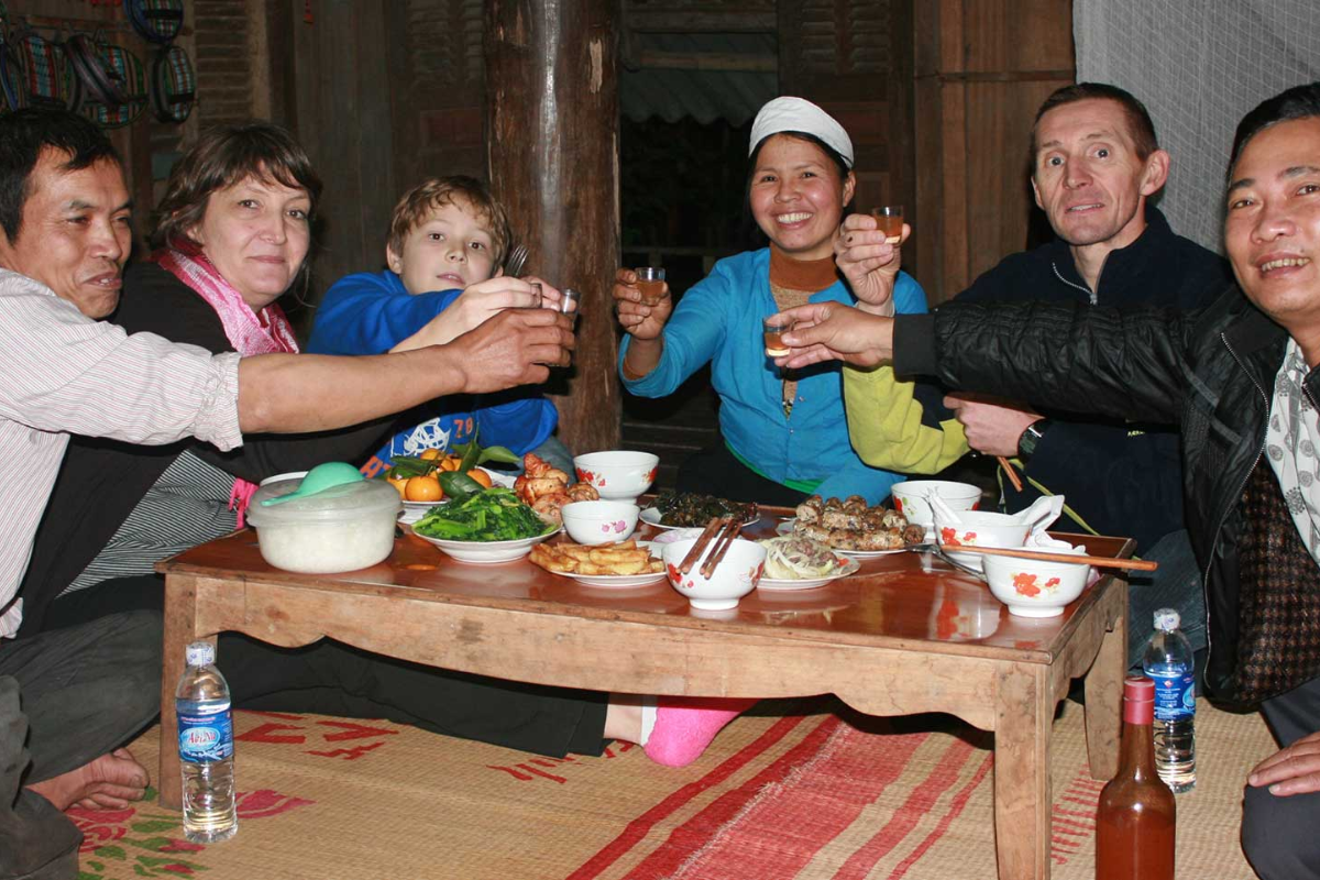 Vietnamese host family sharing a traditional meal with international guests in their home