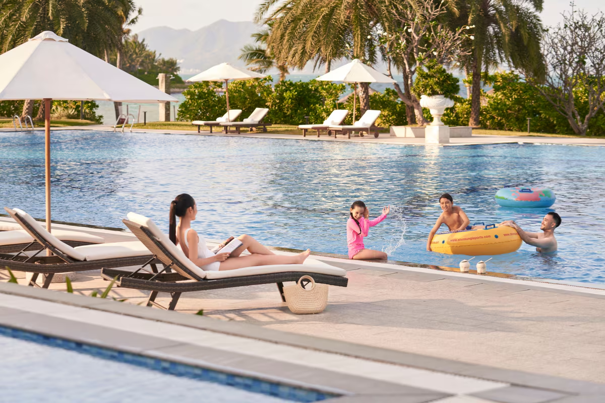 Children splashing in a hotel swimming pool surrounded by palm trees in Vietnam