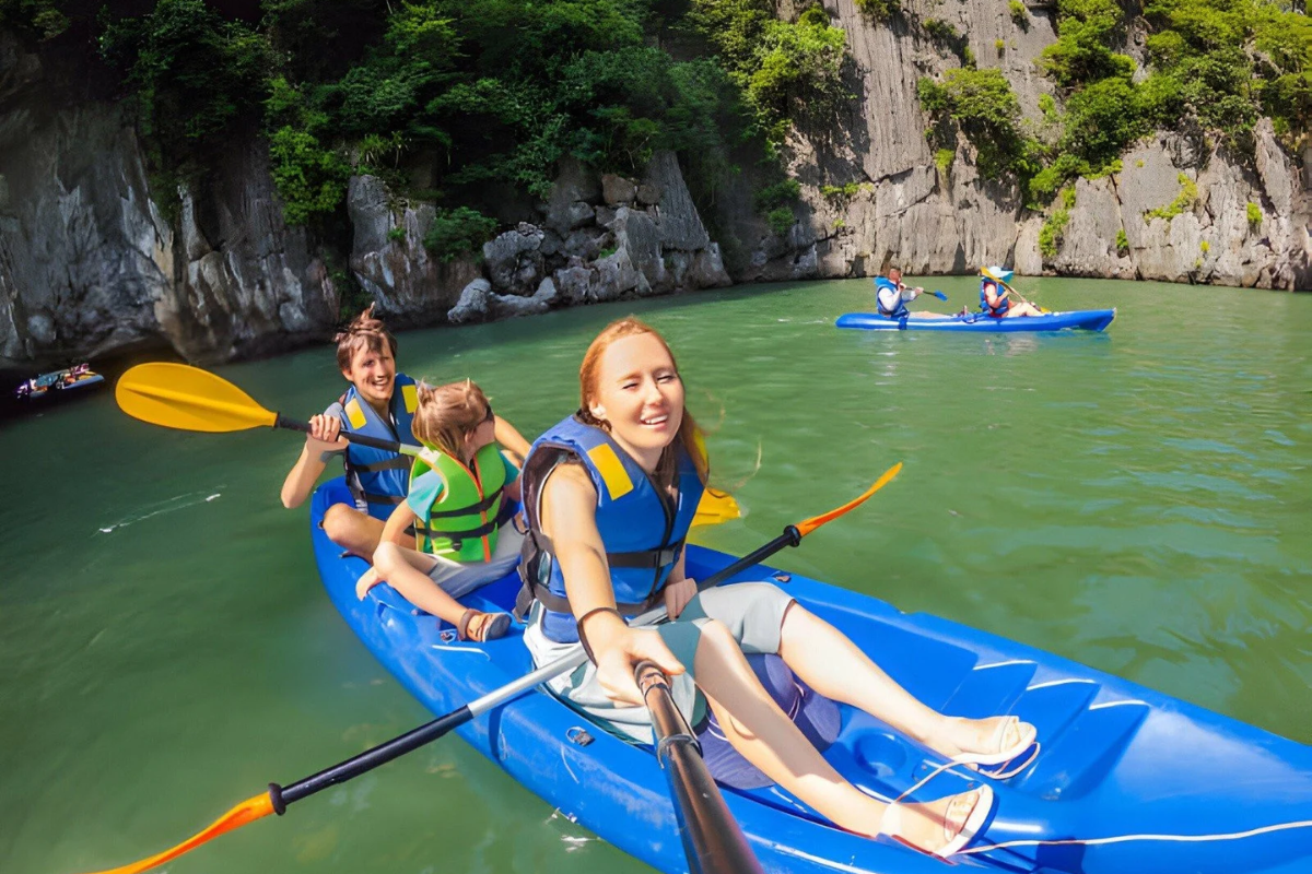 Children kayaking with parents among limestone karsts in Halong Bay at sunset