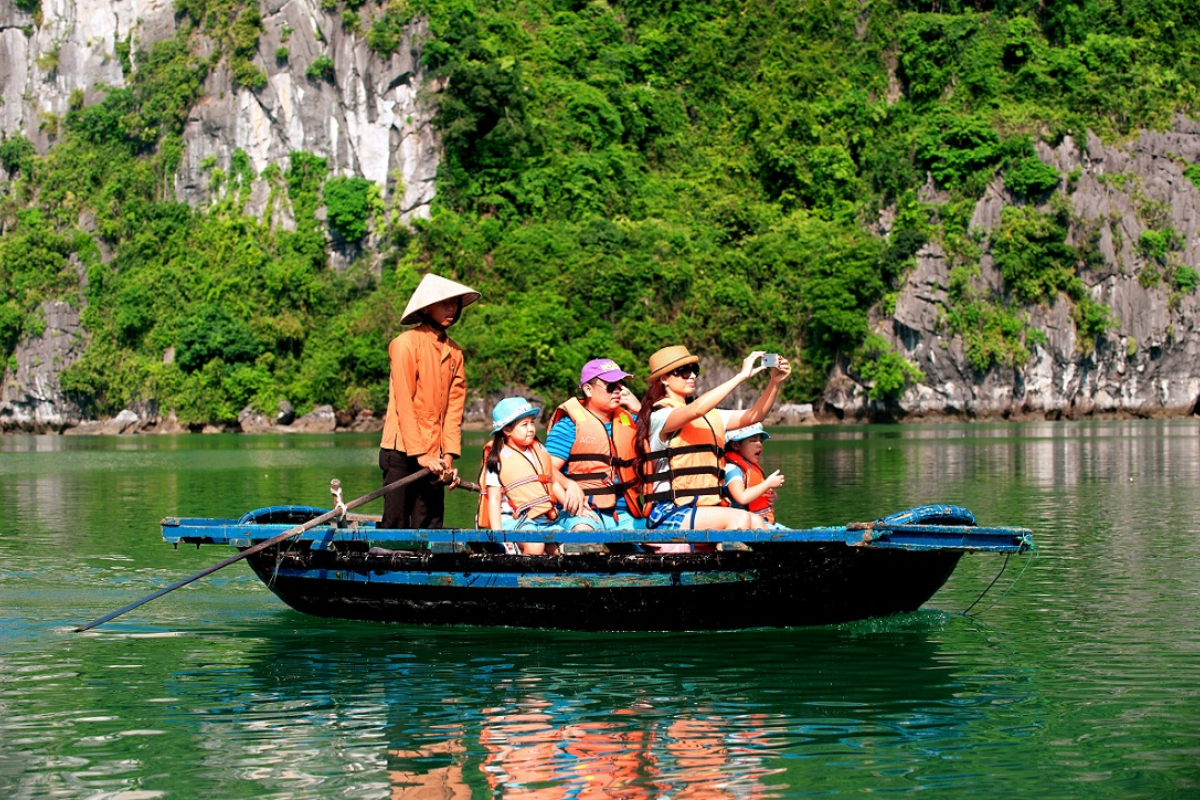 Family riding a sampan boat through lush green rice fields and karst cliffs in Tam Coc
