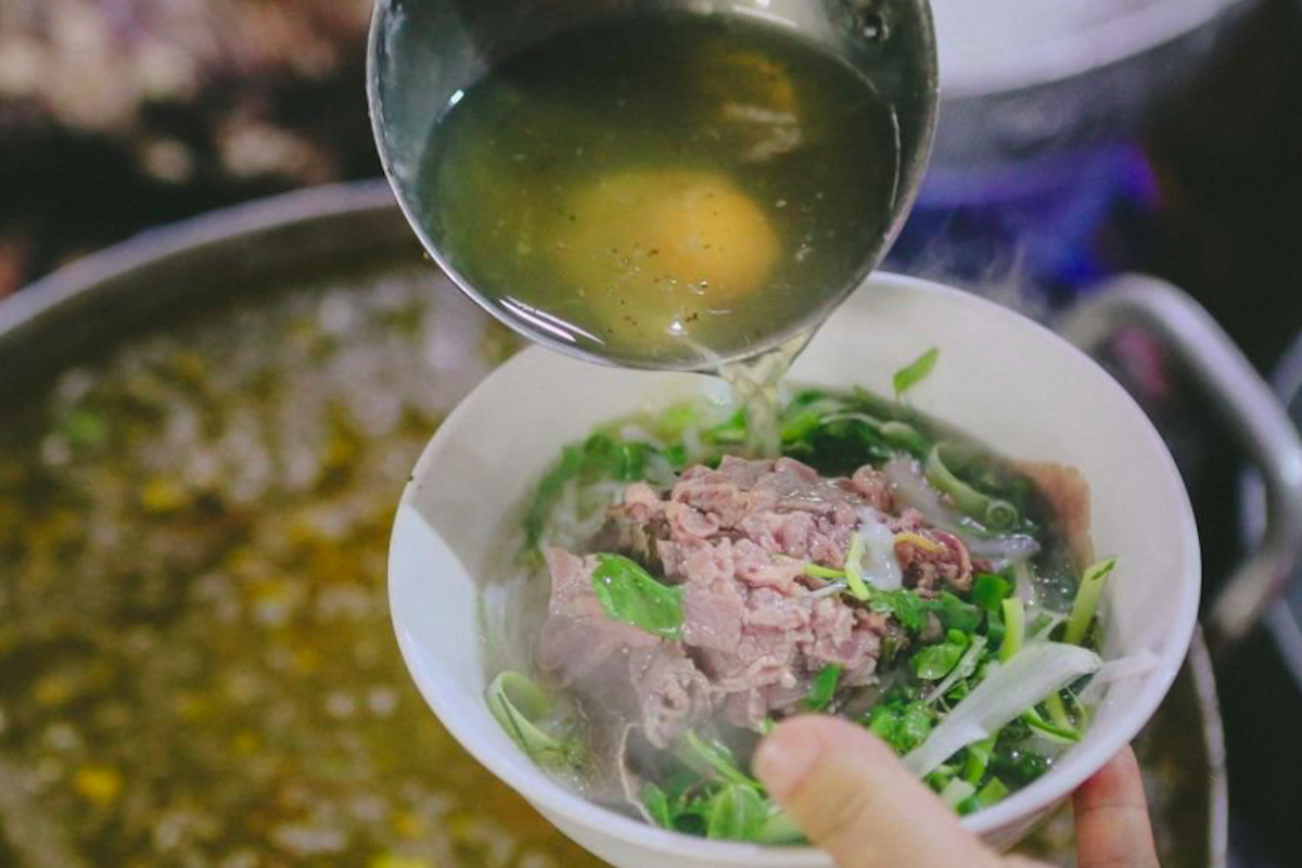 A street vendor in Hanoi preparing Vietnamese noodle soup with fresh herbs and meats