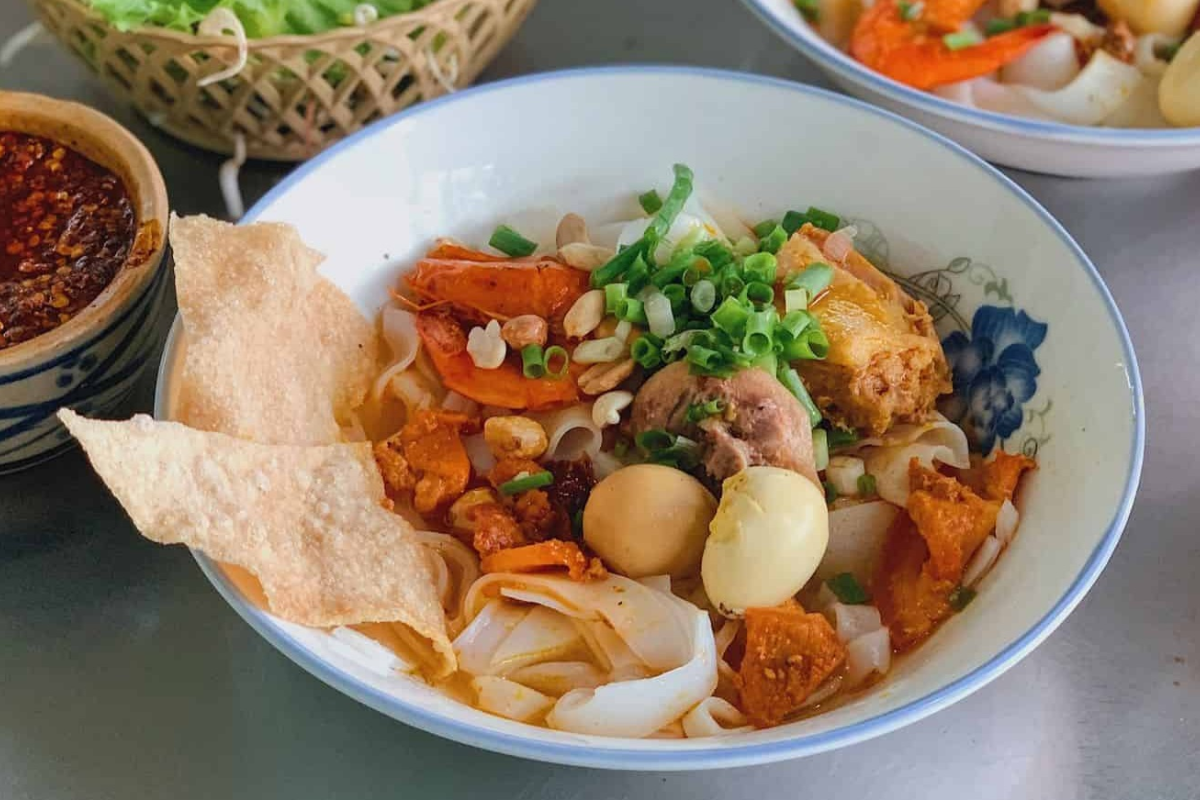 A bowl of Mi Quang garnished with peanuts and fresh greens